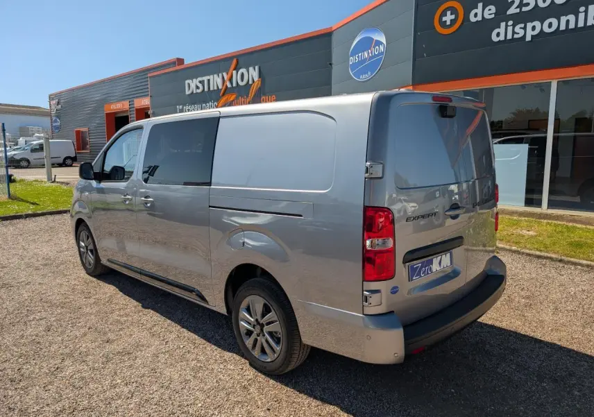 Vue 3/4 arrière droite d'un Peugeot Expert Fourgon gris métallisé avec jantes alliage 17 pouces, stationné devant un bâtiment commercial.