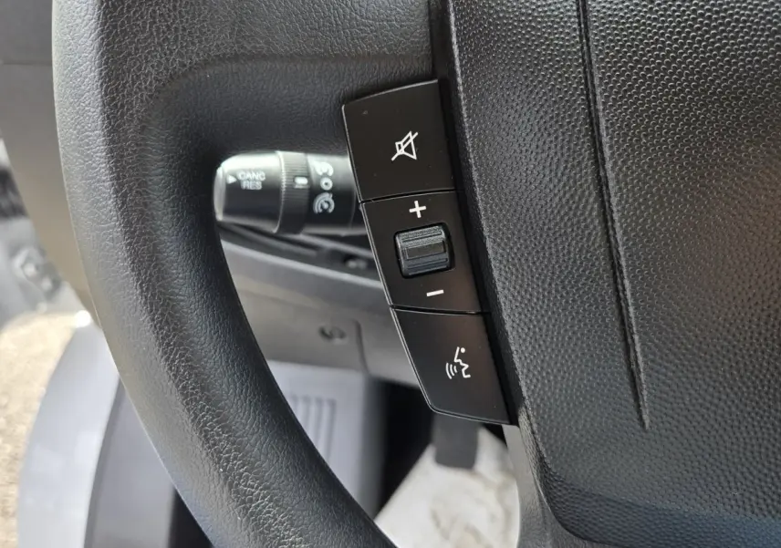 Gros plan sur les commandes du volant noir du Fiat Ducato Fourgon blanc, version 2023, avec régulateur de vitesse.