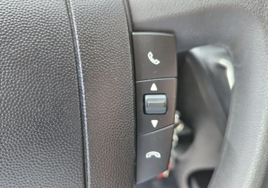 Gros plan sur les commandes de téléphone intégrées au volant noir du Fiat Ducato Fourgon blanc, version 2023.