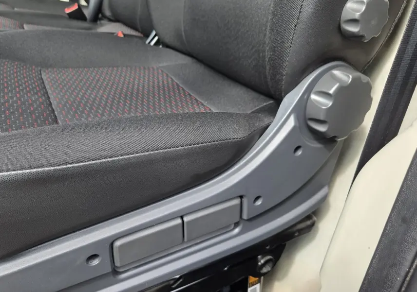 Gros plan sur le réglage manuel du siège conducteur en tissu noir avec motifs rouges du Fiat Ducato Fourgon blanc.