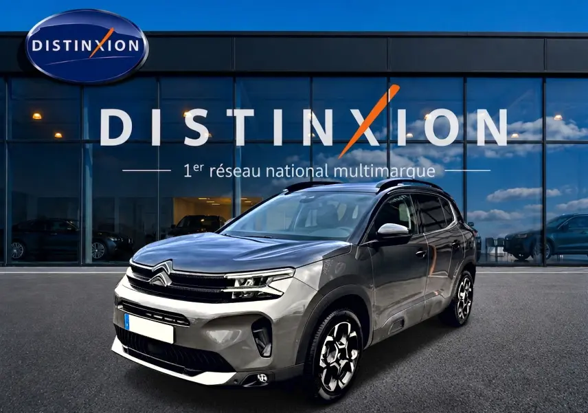Citroën C5 Aircross gris platinium en 3/4 avant droit, avec jantes alu et barres de toit visibles devant showroom Distinxion.