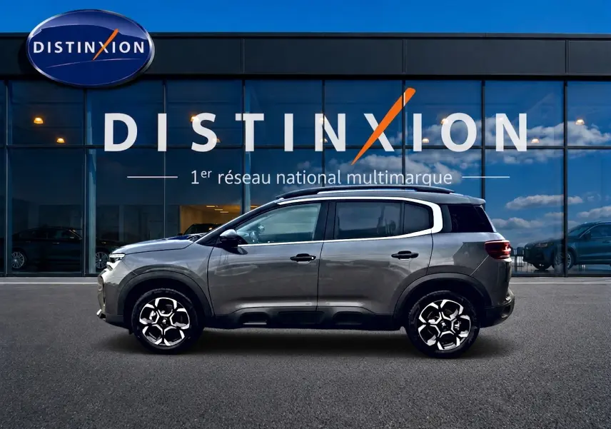 Profil droit du Citroën C5 Aircross gris platinium 2025, avec jantes alu et barres de toit visibles devant vitrine Distinxion.