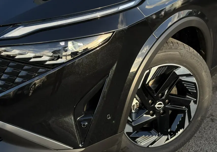 Gros plan sur l'avant droit noir du Nissan Qashqai 2025, mettant en valeur le phare LED et la jante alliage.