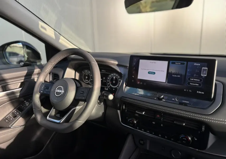 Vue intérieure côté conducteur du Nissan Qashqai 2025 noir, avec volant cuir et écran tactile large sur tableau de bord.