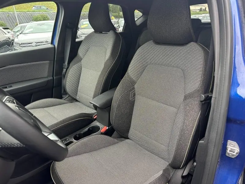 Vue intérieure avant du Renault Captur bleu Iron, sièges tissu gris avec accoudoir central et console entre les sièges.