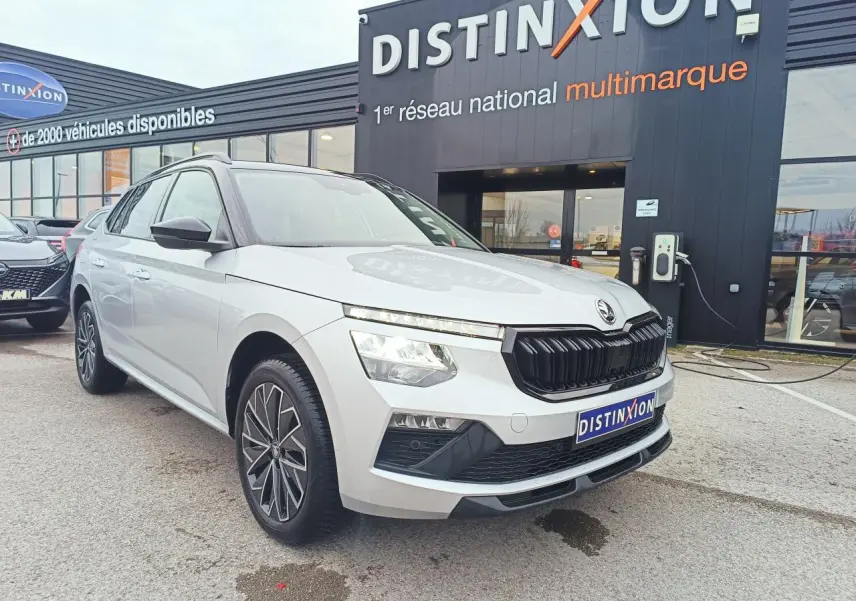 Vue 3/4 avant d’un Skoda Kamiq 2025 argent avec toit noir et jantes alliage 17 pouces, devant un showroom Distinxion.