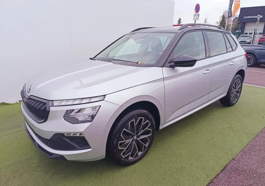 Vue 3/4 avant d'un Skoda Kamiq 2025 argent avec toit noir et jantes alliage 17 pouces, stationné sur sol vert.