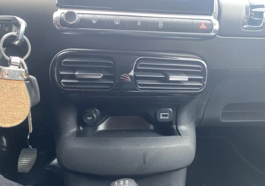 Vue rapprochée de la console centrale noire avec aérateurs, prise 12V, port USB et levier de vitesses manuel d'une Citroën C4 Cactus.