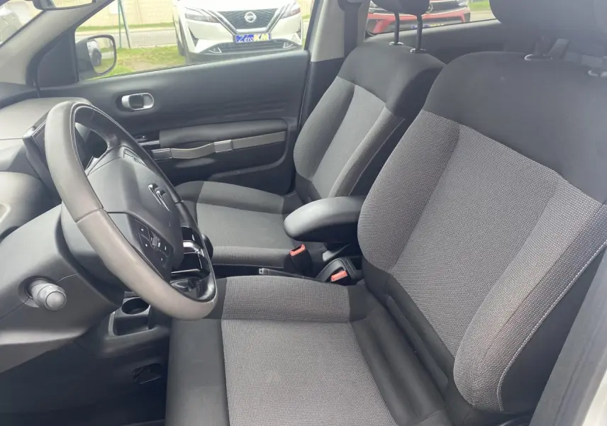 Vue intérieure côté conducteur de la Citroën C4 Cactus blanche de 2015, montrant sièges tissu gris et volant multifonction.