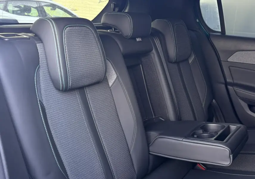 Vue intérieure des sièges arrière de la Peugeot 308 2024, sellerie tri matières noire avec surpiqûres bleues et accoudoir central déplié.