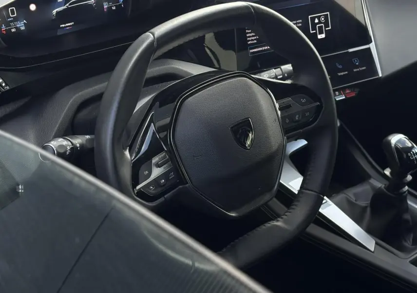 Vue intérieure rapprochée du volant cuir noir et levier de vitesse manuel de la Peugeot 308 2024.