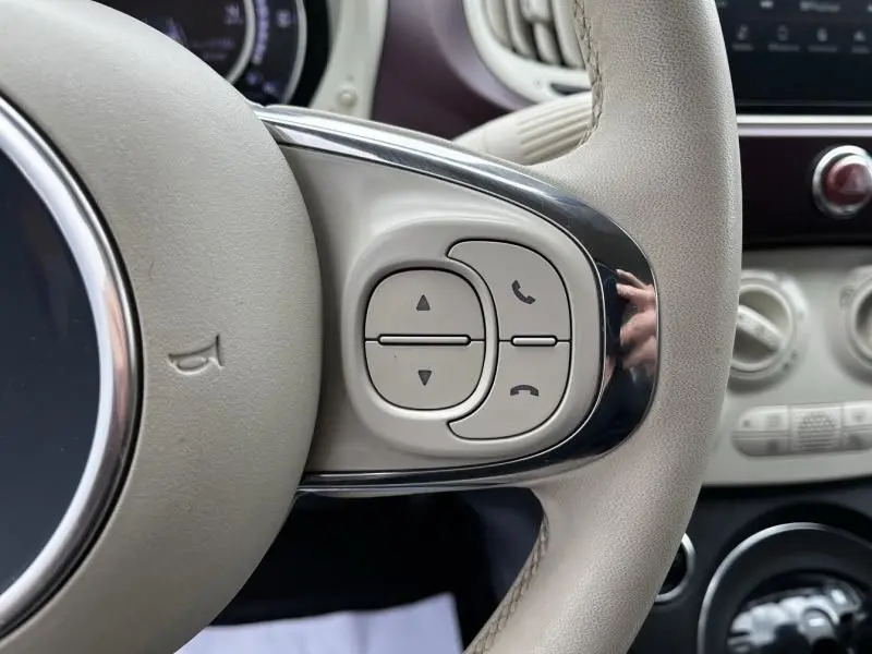 Gros plan sur les commandes de téléphone et volume sur le volant beige de la Fiat 500C blanche 2020.
