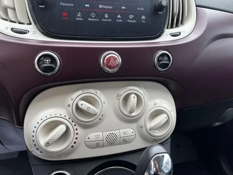 Gros plan sur la console centrale bordeaux et blanche du tableau de bord de la Fiat 500C blanche, avec commandes de climatisation et écran tactile.
