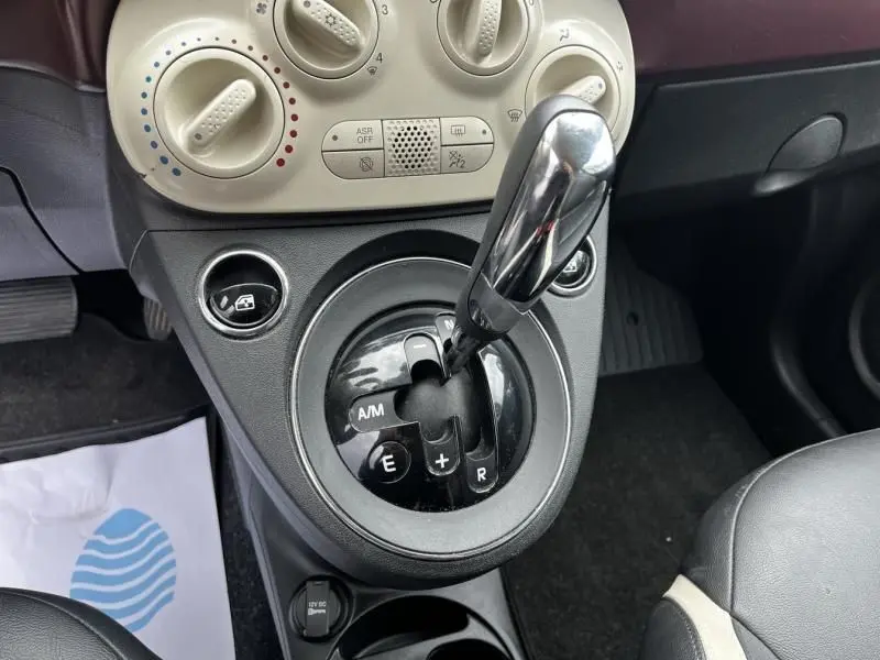 Gros plan sur la console centrale de la Fiat 500C blanche, mettant en valeur le levier de vitesse automatique et les commandes de climatisation.