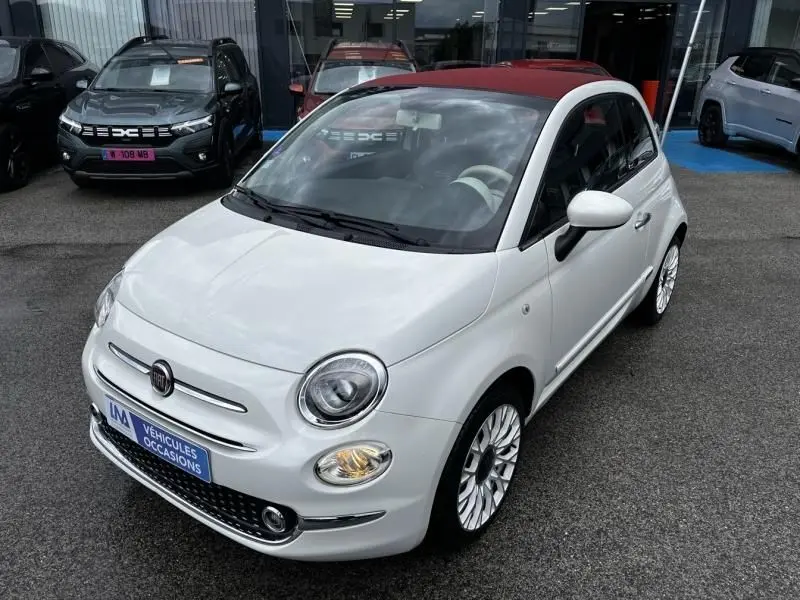 Vue 3/4 avant droite d'une Fiat 500C blanche avec toit rouge, jantes multibranches et feux allumés.