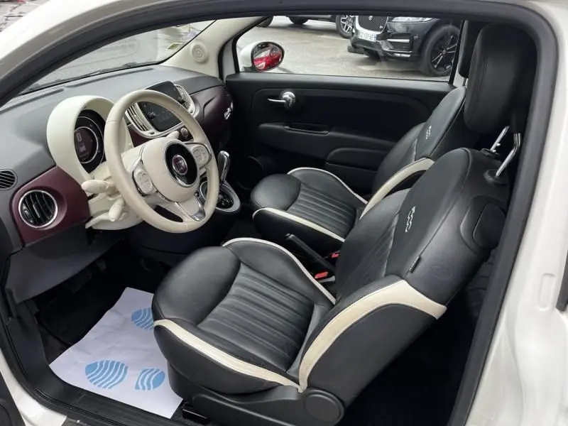Vue intérieure côté gauche de la Fiat 500C blanche 2020, sièges noirs avec surpiqûres blanches et tableau de bord bicolore.