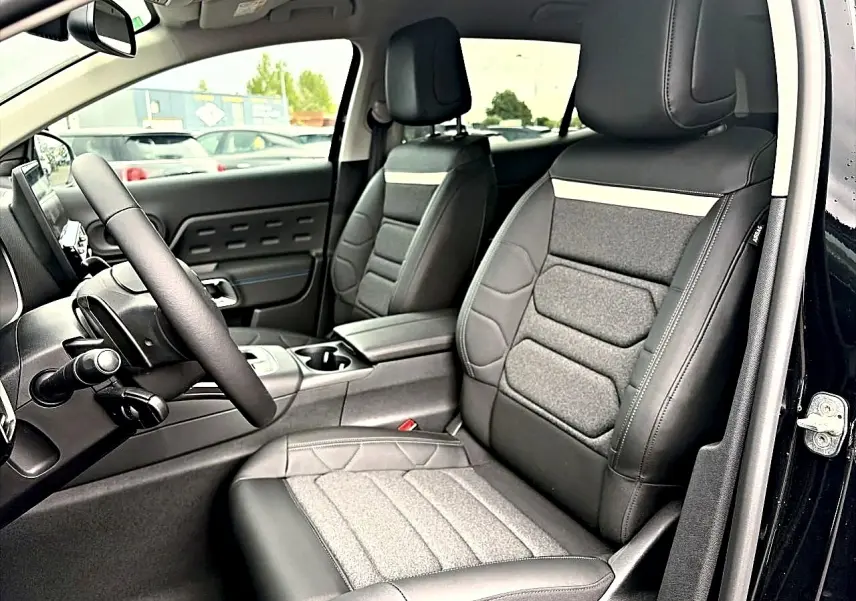 Vue intérieure côté conducteur du Citroën C5 Aircross noir 2025, sièges en cuir et tissu avec accoudoir central.