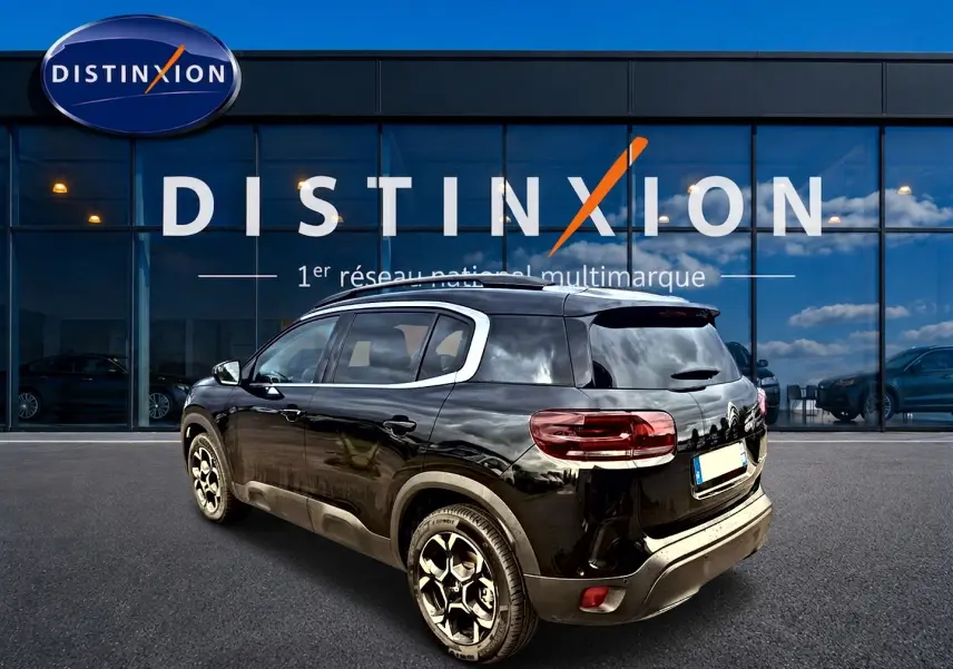 Vue 3/4 arrière droite d'un Citroën C5 Aircross noir avec jantes alu devant une vitrine Distinxion.