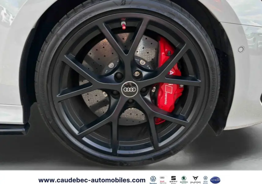 Gros plan sur la jante noire mat à 5 branches en Y de l'Audi RS3 Sportback grise avec étrier de frein céramique rouge visible.