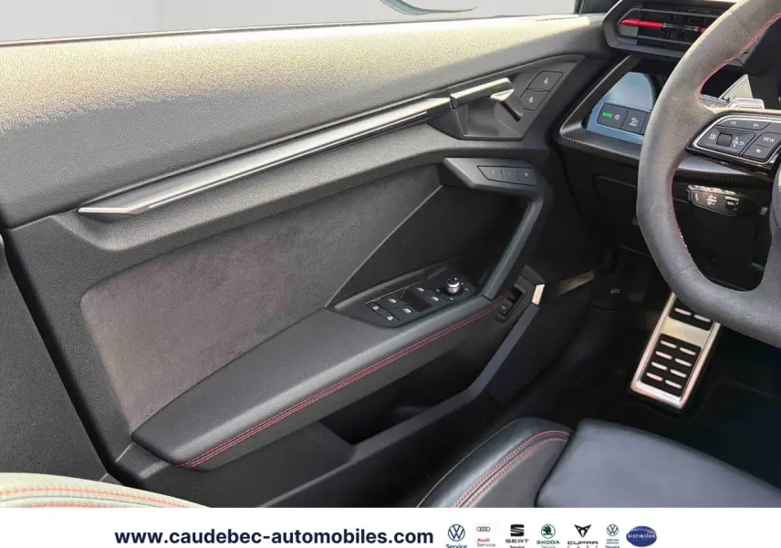 Vue intérieure côté conducteur de l'Audi RS3 Sportback 2022, avec garniture noire et surpiqûres rouges visibles sur la porte et le volant.