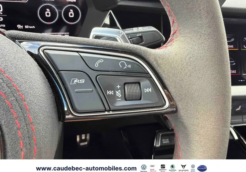Gros plan sur le volant en cuir avec surpiqûres rouges et commandes RS d'une Audi RS3 Sportback grise, intérieur moderne.