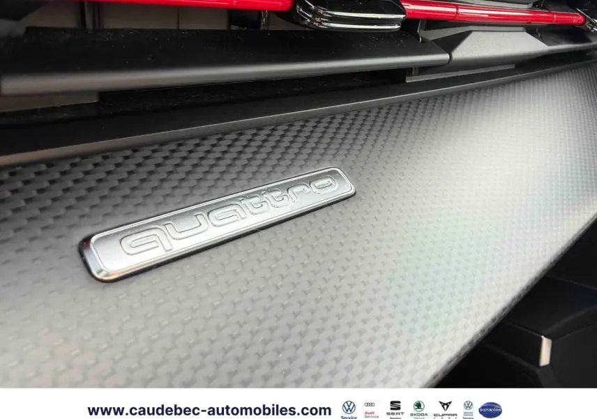 Détail intérieur du tableau de bord en carbone avec logo Quattro argenté et éléments rouges sur Audi RS3 Sportback.