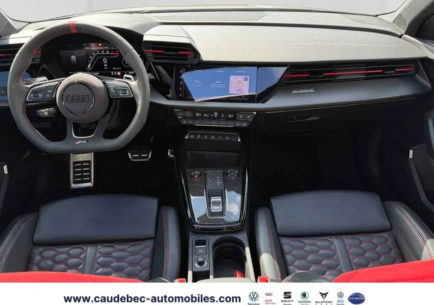 Vue intérieure avant de l’Audi RS3 Sportback 2022 avec volant sport, surpiqûres rouges et inserts carbone sur la console centrale.