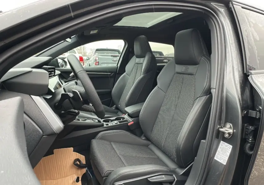 Vue intérieure côté conducteur de l'Audi A3 gris Daytona, sièges sport cuir-tissu avec logo S et toit panoramique.