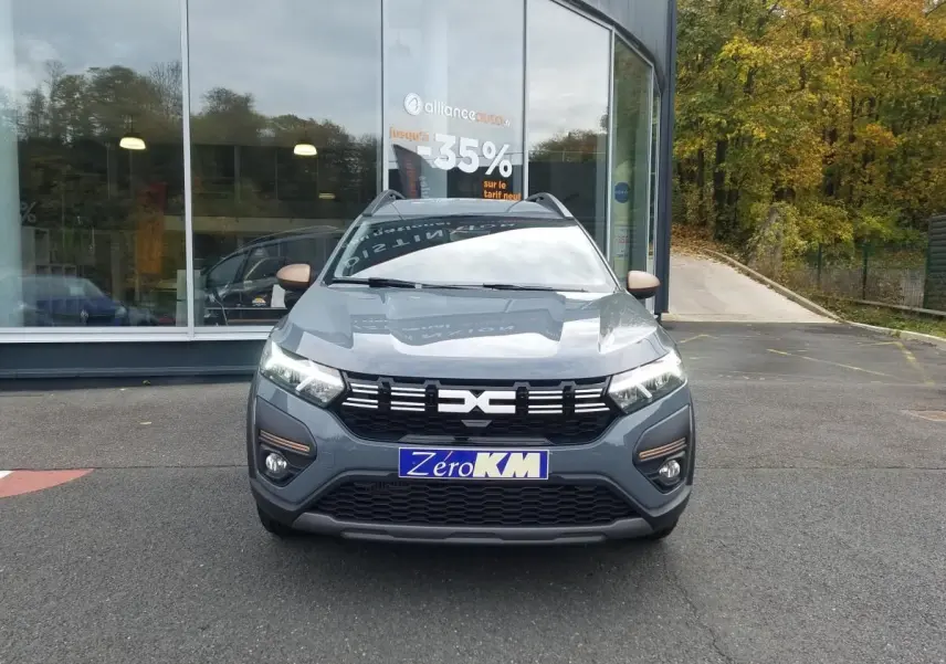 Vue frontale d'un Dacia Jogger gris urbain 2025 avec feux LED allumés et barres de toit visibles.