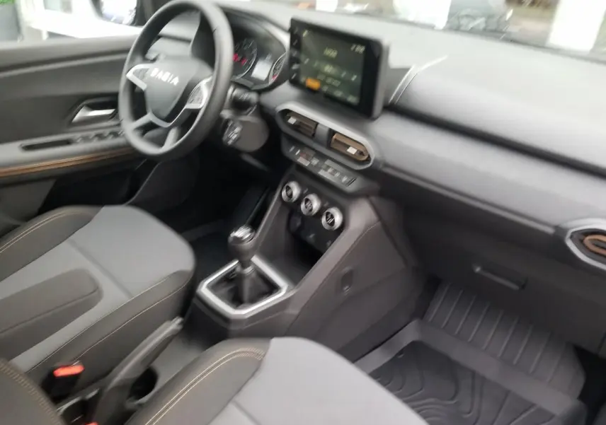 Intérieur du Dacia Jogger 2025 vu côté conducteur, sièges gris avec surpiqûres, tableau de bord et écran tactile central.