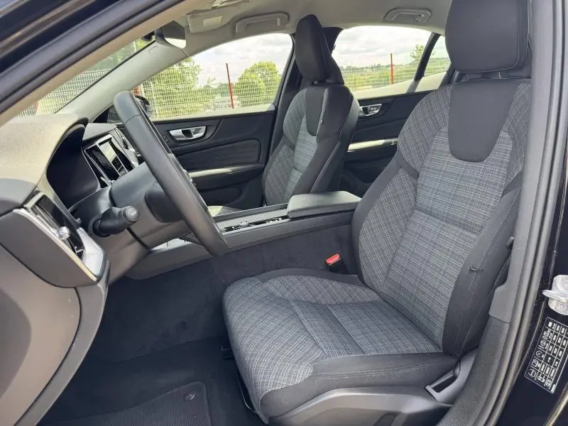 Vue intérieure côté conducteur du Volvo S60 2024 avec sièges tissu gris à motifs et tableau de bord noir.