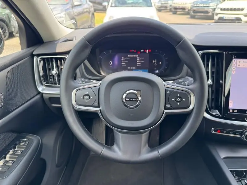 Vue intérieure centrée sur le volant noir du Volvo S60 2024 avec tableau de bord numérique et écran tactile latéral.