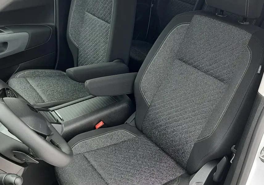 Vue intérieure côté conducteur du Peugeot Rifter 2026 blanc Kaolin, sièges tissu gris avec accoudoir central.