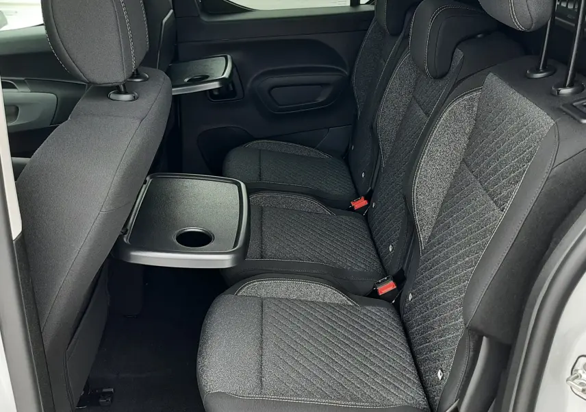 Vue latérale intérieure des sièges arrière gris foncé du Peugeot Rifter blanc Kaolin 2026 avec tablette rabattable.