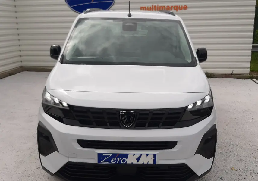 Vue avant d'un Peugeot Rifter blanc Kaolin 2026 avec calandre noire et phares LED allumés, immatriculé Zero KM.