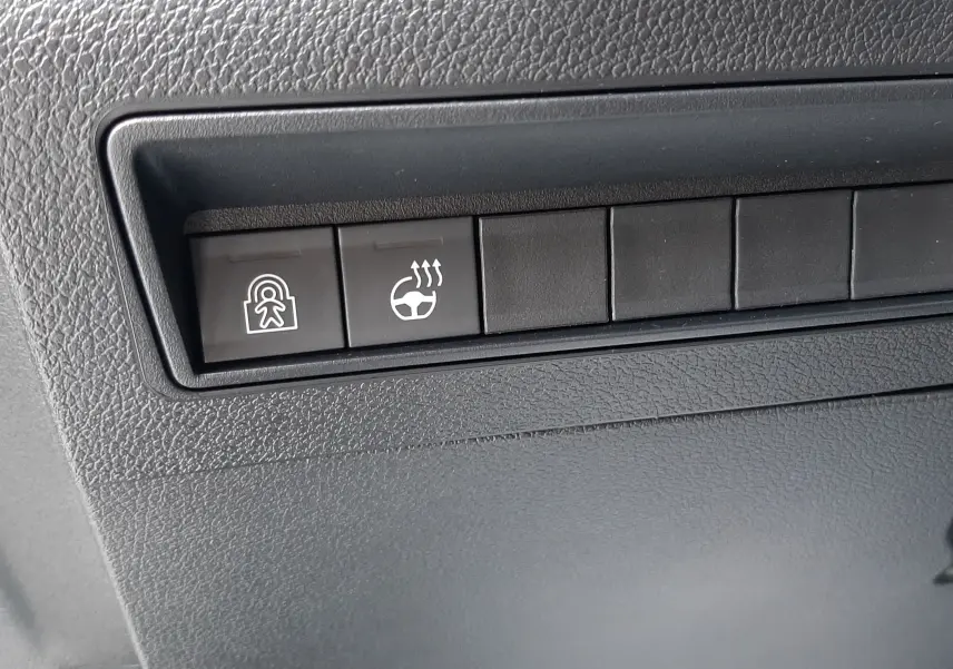 Gros plan sur les boutons de commande du volant chauffant et de sécurité dans l’habitacle gris du Peugeot Rifter blanc Kaolin.