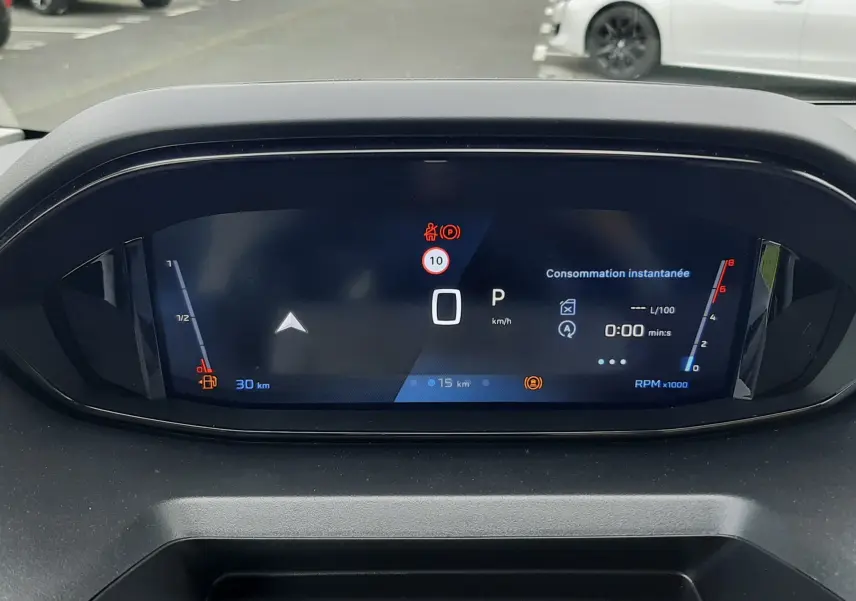Vue rapprochée du tableau de bord numérique du Peugeot Rifter blanc Kaolin, affichant la consommation instantanée et la vitesse à 0 km/h.
