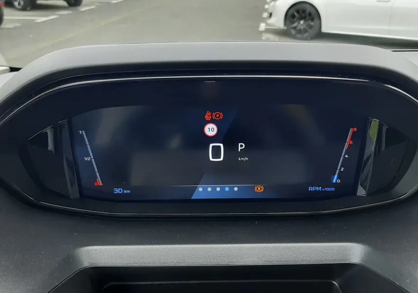 Vue rapprochée du tableau de bord numérique du Peugeot Rifter blanc Kaolin, affichant la vitesse à 0 km/h et le mode parking.