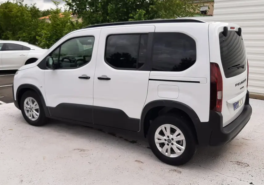 Peugeot Rifter blanc Kaolin vu en 3/4 arrière côté gauche, avec vitres teintées et protections noires basses.