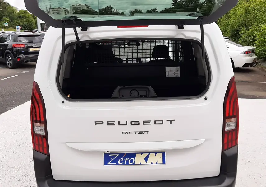 Vue arrière d'un Peugeot Rifter blanc Kaolin 2026 avec hayon ouvert, montrant l'espace de chargement et la grille de séparation.