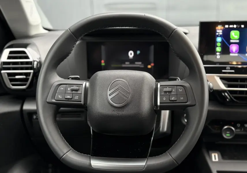Vue centrée sur le volant cuir noir de la Citroën C4 Hybrid 2025 avec commandes intégrées et tableau de bord numérique.