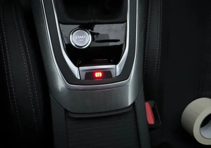 Gros plan sur la console centrale de la Peugeot 308 gris Artense, montrant le bouton start et le frein de parking électrique allumé.