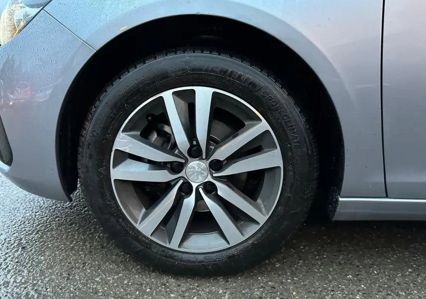 Gros plan sur la roue avant gauche d'une Peugeot 308 gris Artense avec jante alliage et carrosserie humide.