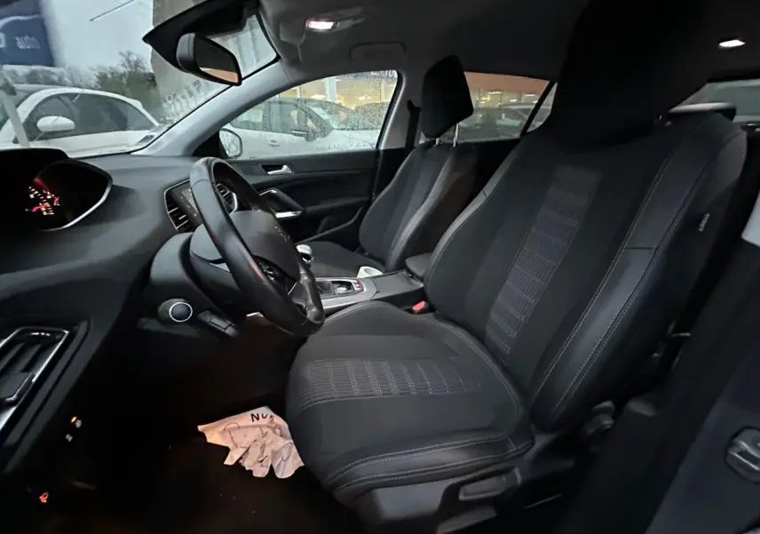 Intérieur avant de la Peugeot 308 gris Artense, vue côté conducteur, sièges tissu noir et tableau de bord visible.