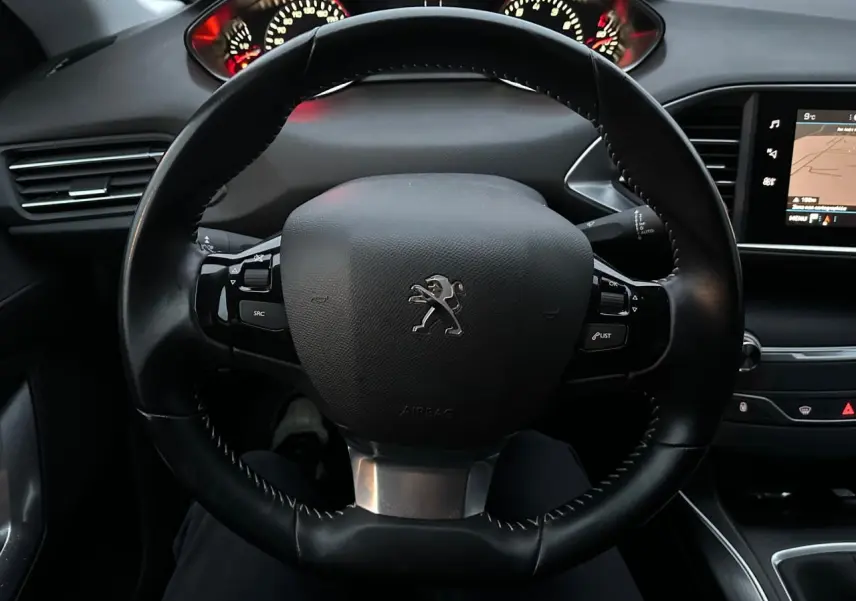 Vue intérieure centrée sur le volant noir de la Peugeot 308 avec tableau de bord et écran tactile visible à droite.