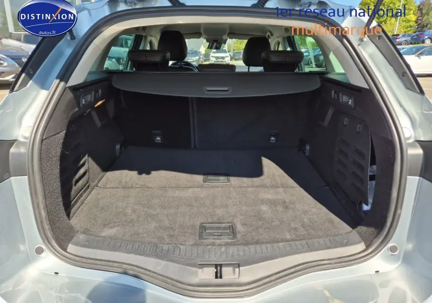 Coffre ouvert vu de l'arrière d'une Renault Mégane Break gris titanium, montrant l'espace de chargement et banquette arrière.
