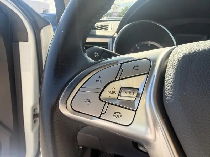 Gros plan sur les commandes au volant côté gauche du SsangYong Tivoli blanc 2017, avec boutons volume et mode audio.