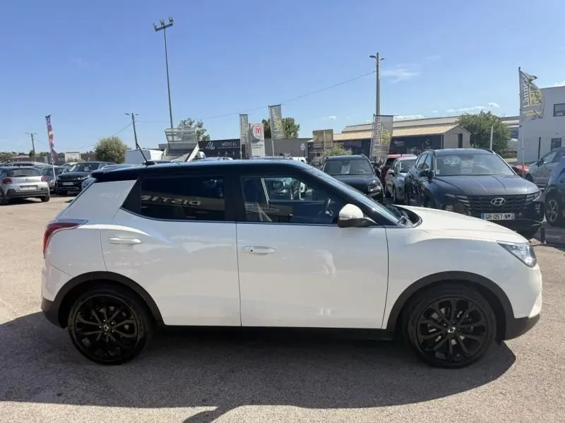 Vue de profil côté gauche d’un SsangYong Tivoli blanc bi-ton avec toit noir et jantes noires sur parking extérieur.