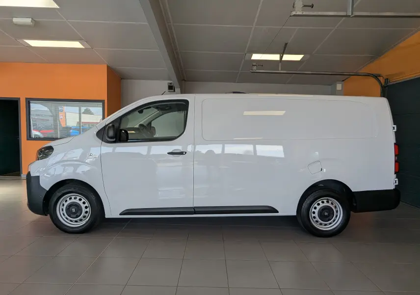 Vue de profil côté gauche d’un FIAT Scudo Fourgon XL 145 blanc, avec jantes tôles 16 pouces, dans un garage.
