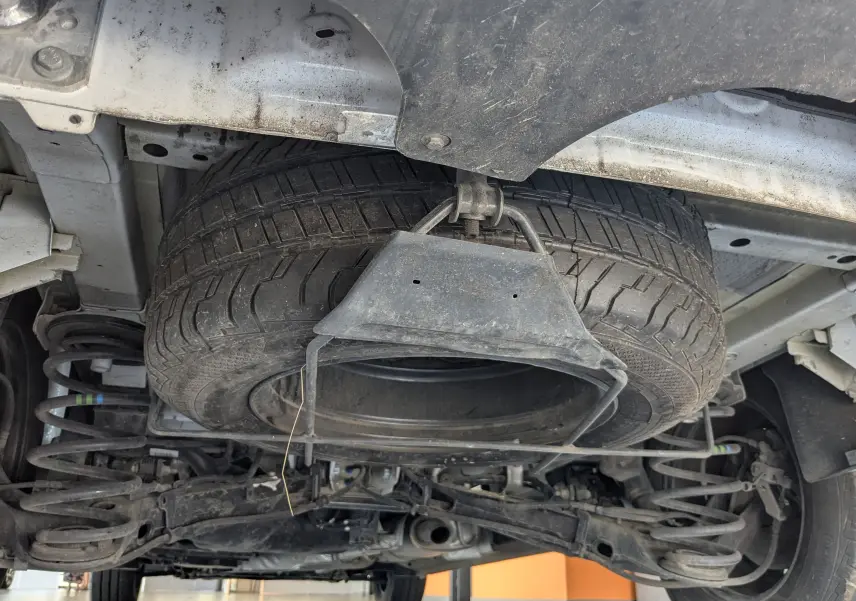 Vue en contre-plongée sous un FIAT Scudo Fourgon blanc 2024, montrant la roue de secours suspendue sous le châssis.